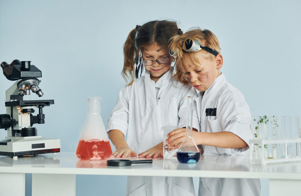 Little girl and boy in white coats plays a scientists in lab by using equipment